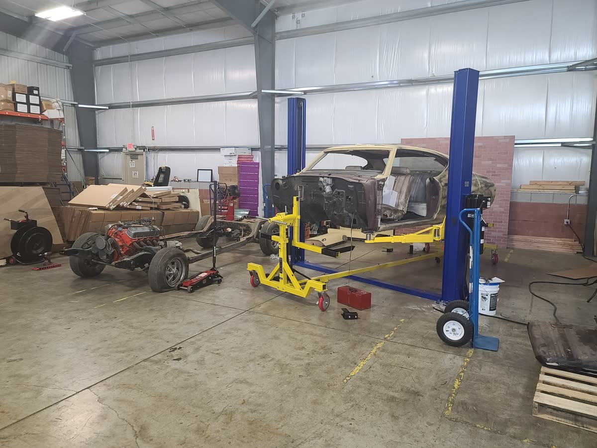 Body shell on the lift beside its rolling chassis during a frame-off phase